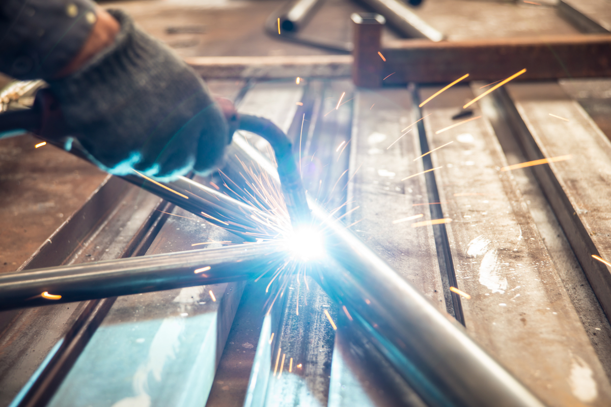 Close up view of gloved hands holding a welding torch welding a pipe on a table. 