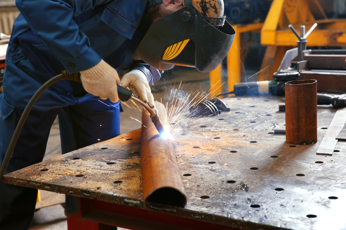 Welder working on a metal pipe in a welding shop